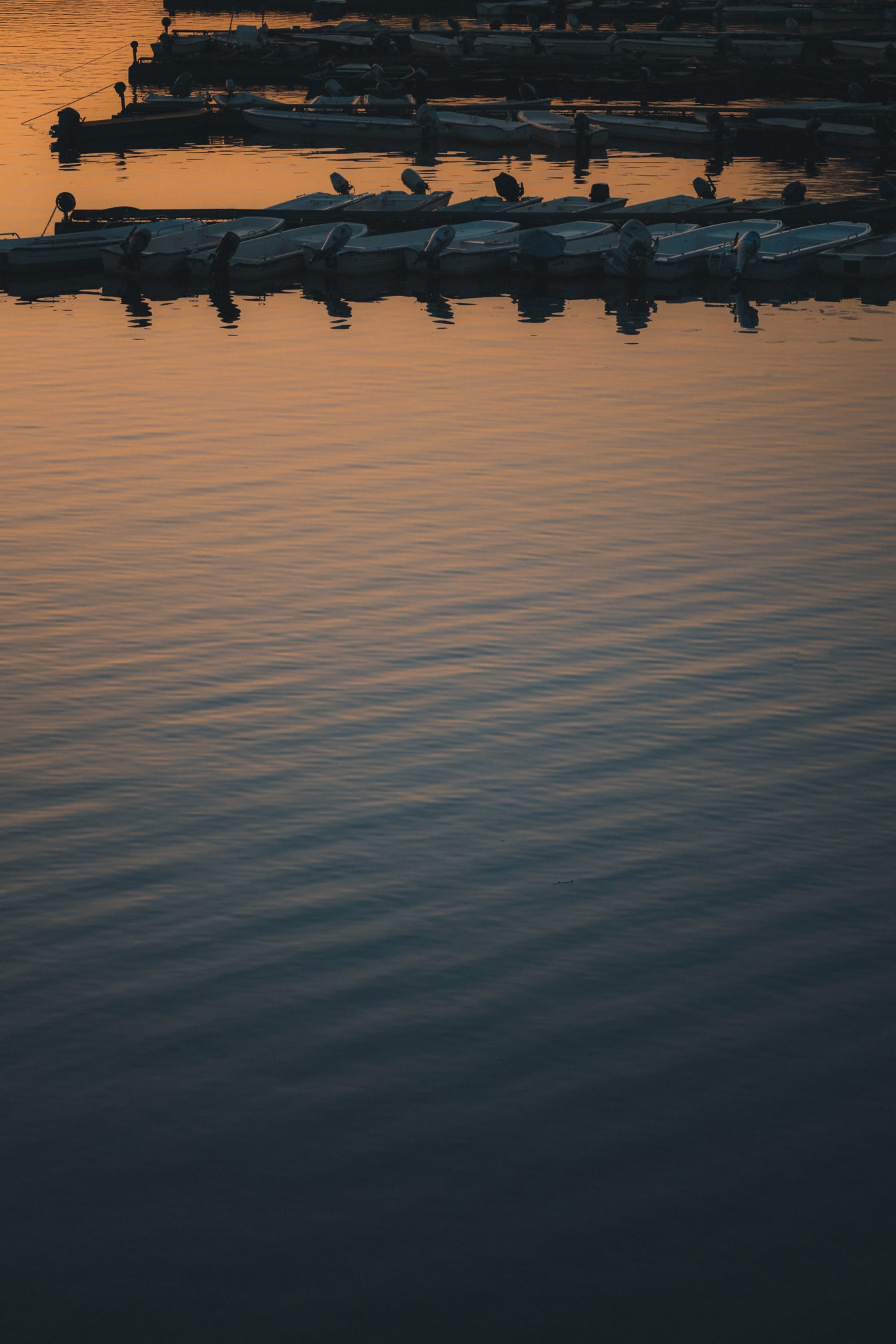 Mirna vodena površina sa siluetom ribarskih brodova u luci u sumrak