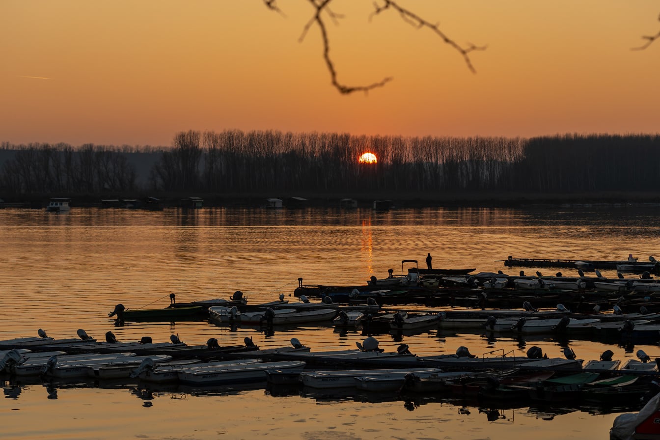 Silueta rybářských lodí v přístavu při západu slunce nad jezerem