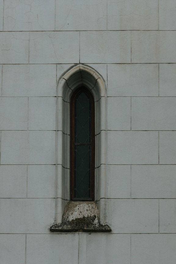 Schmales kleines Fenster im gotischen Stil auf weißer Steinmauer