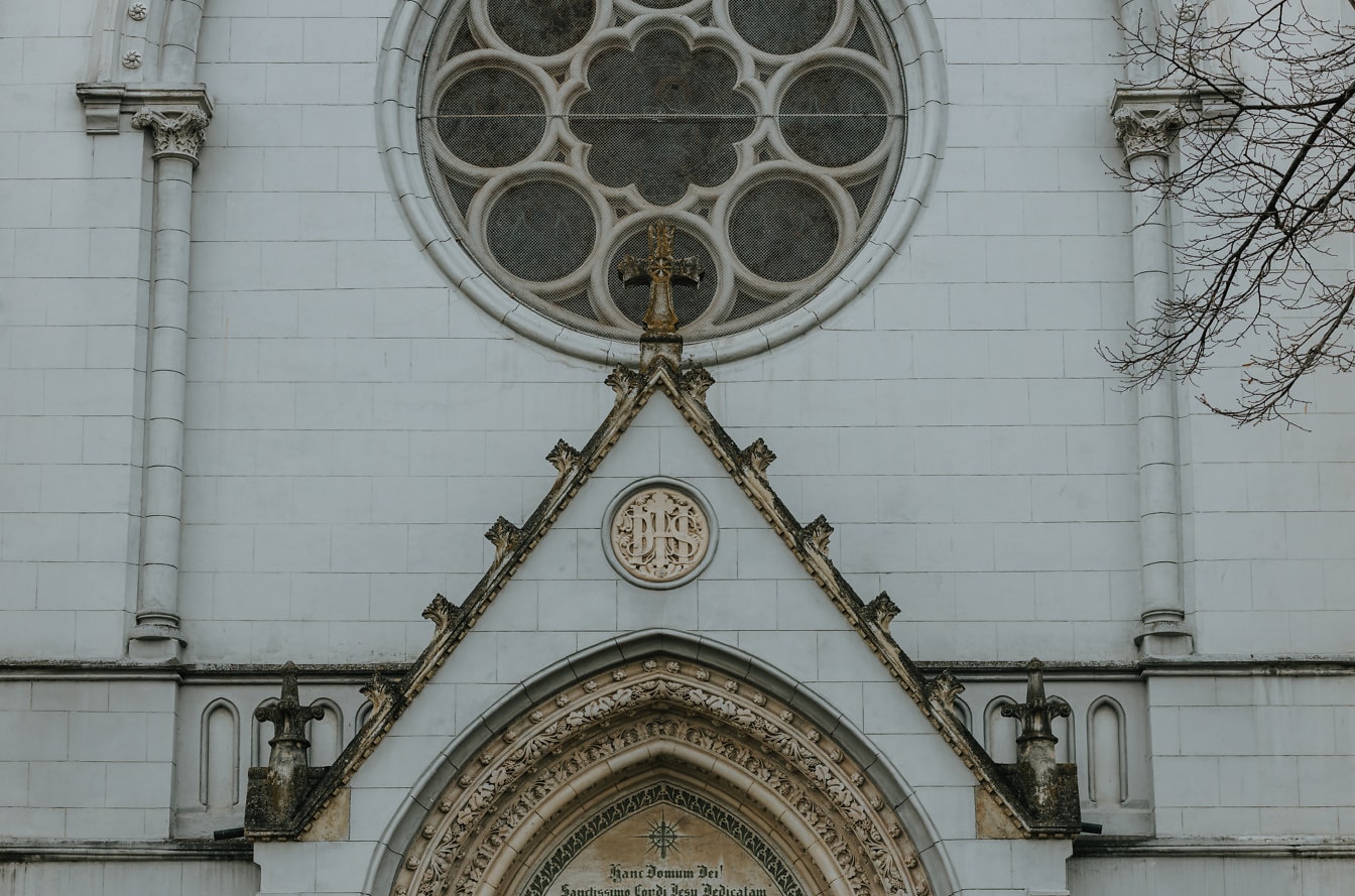 Špinavý kamenný kríž na streche pri vchode do gotickej katedrály