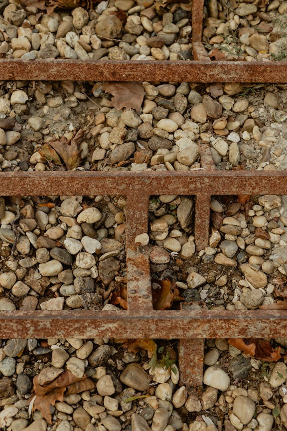 Rusten jernkonstruksjon av metalltrapp på småstein