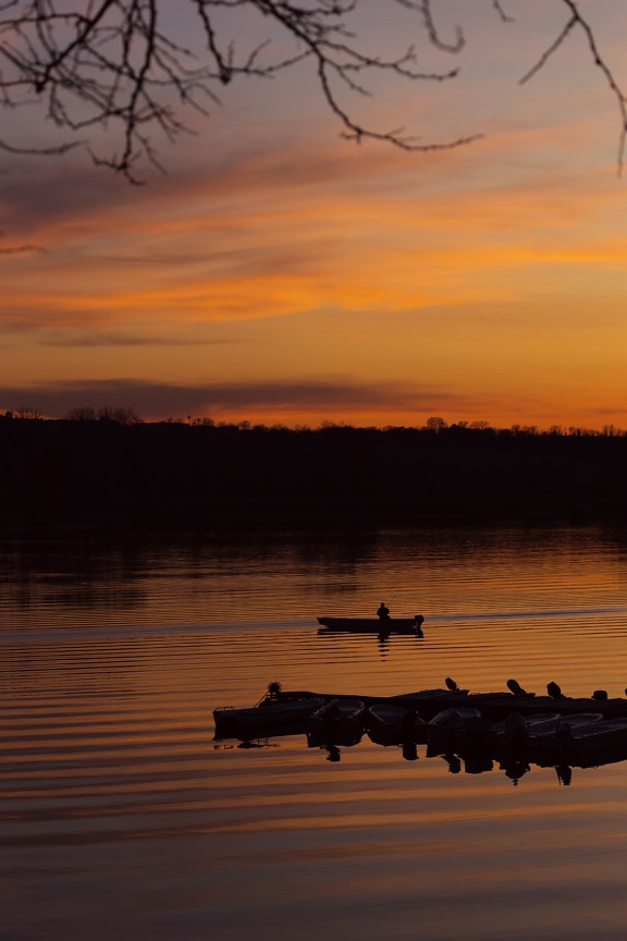 Orange yellow dramatic sunrise on lakeside with silhouette of fishing boat