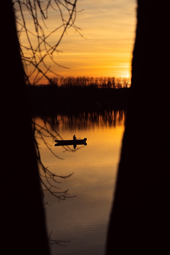 Silhouette of fisherman in fishing boat on orange-yellow sunset