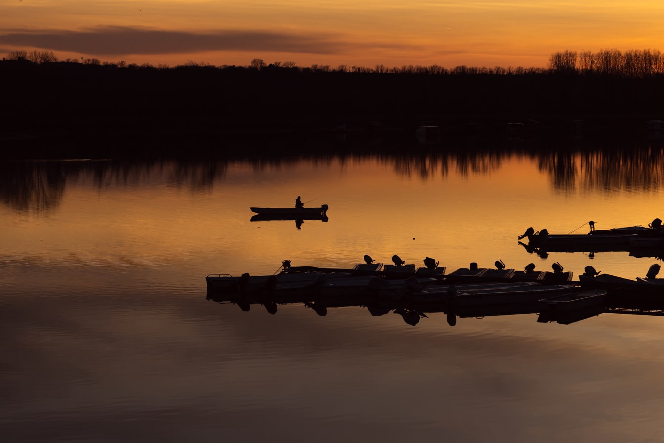 Silueta rybárskych lodí v prístave jazera pri oranžovo-žltom východe slnka