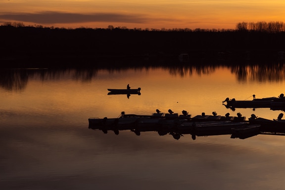 Silhouette of fishing boats in lake harbor at orange-yellow sunrise