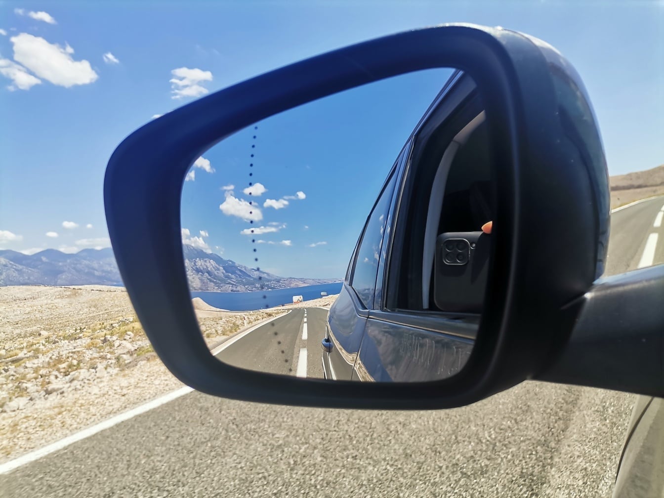 Reflexia asfaltului, a drumului și a peisajului marin în oglinda mașinii