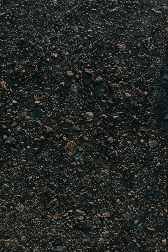Dark granite pebbles on rough ground texture