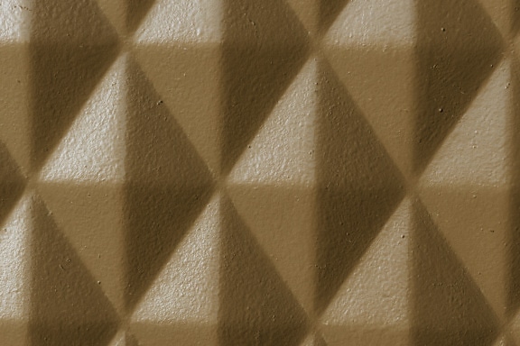 Yellowish brown paint on geometric rhomb pattern metal texture close-up