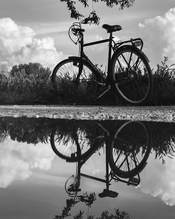 Monochrome photo of bicycle on countryside road with reflection on water