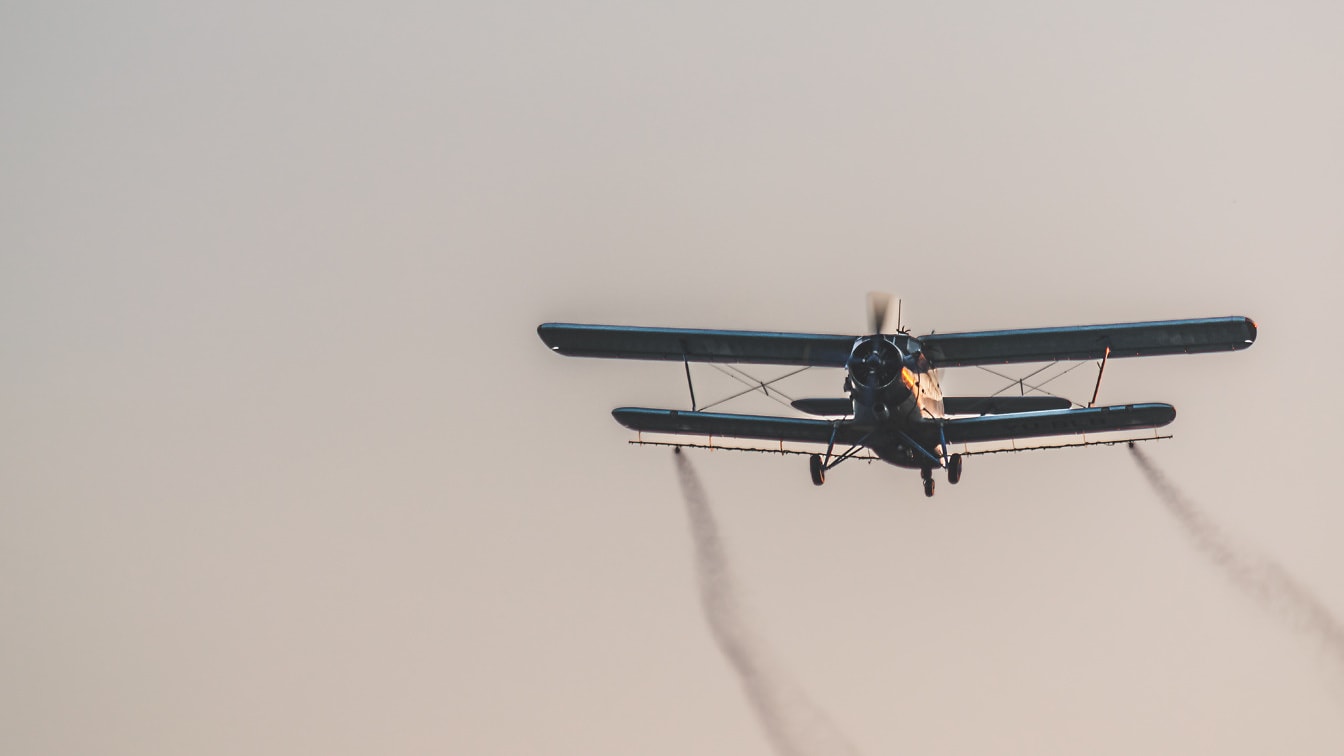Avión biplano anticuado que vuela en el cielo y fumiga