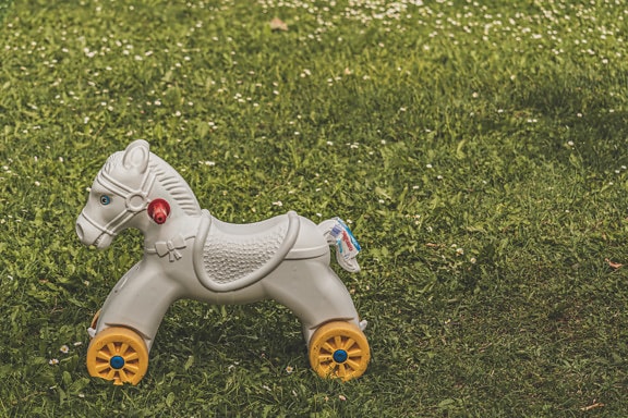 Hvid legetøjshest af plast med gullige hjul på græsplænen