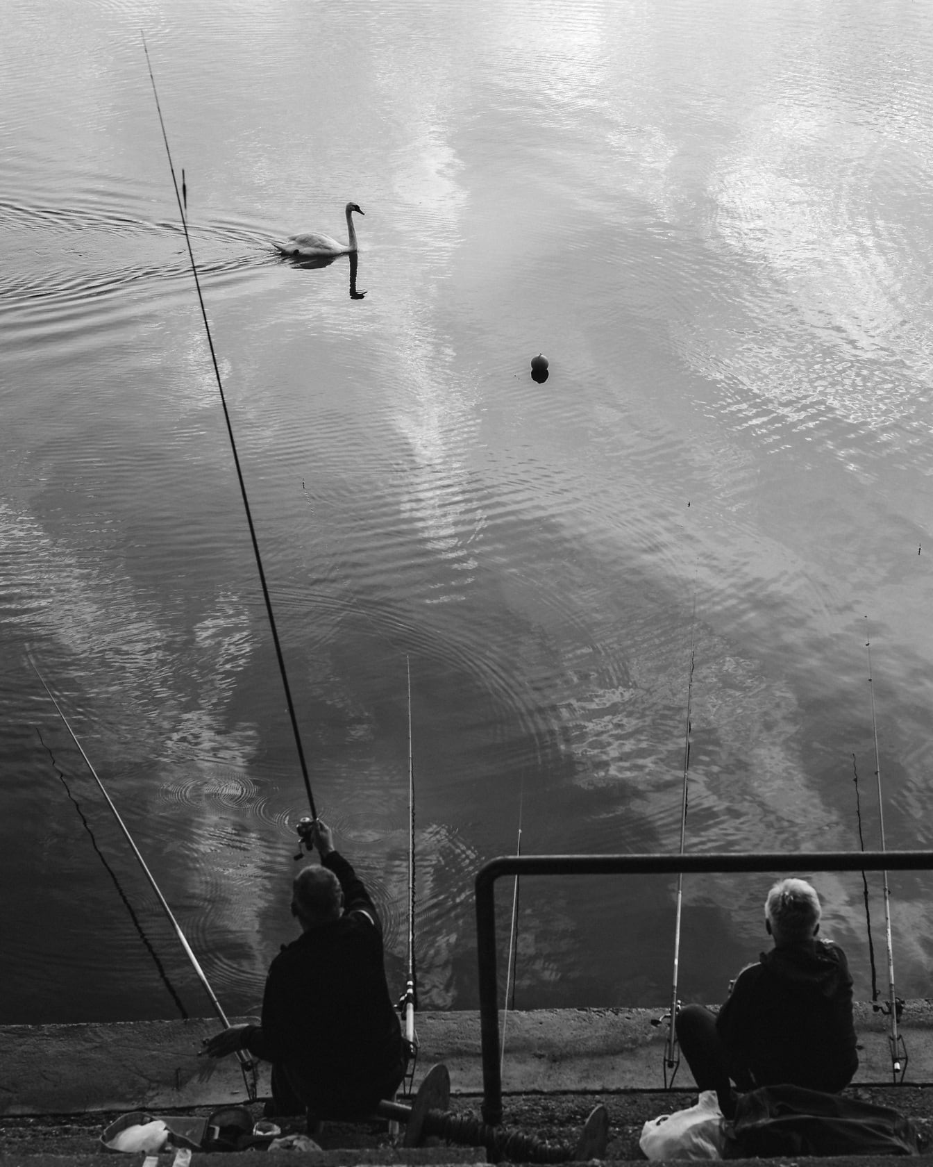 Rybár sediaci na schodisku a rybárčiaci s rybárskym prútom