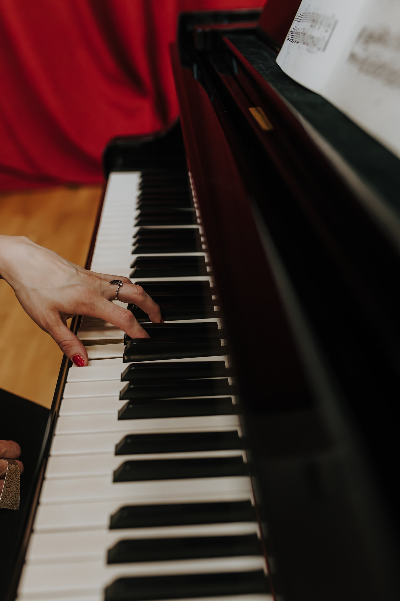 ภาพระยะใกล้ของมือพร้อมแหวนทองและยาทาเล็บสีแดงเล่นเปียโน