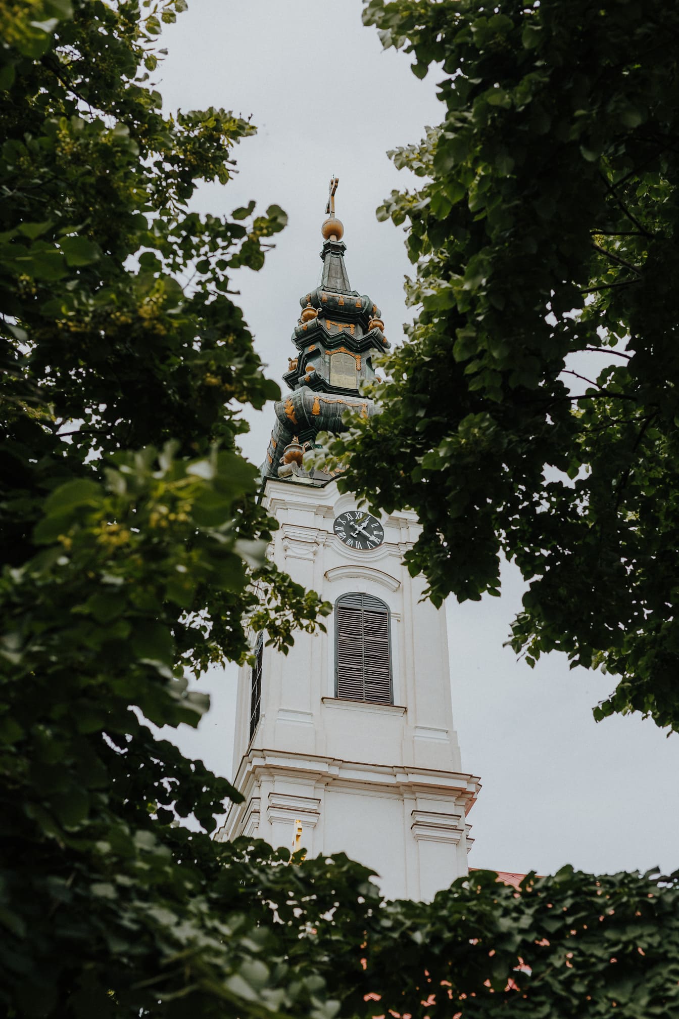 Turnul bisericii ortodoxe albe printre copaci