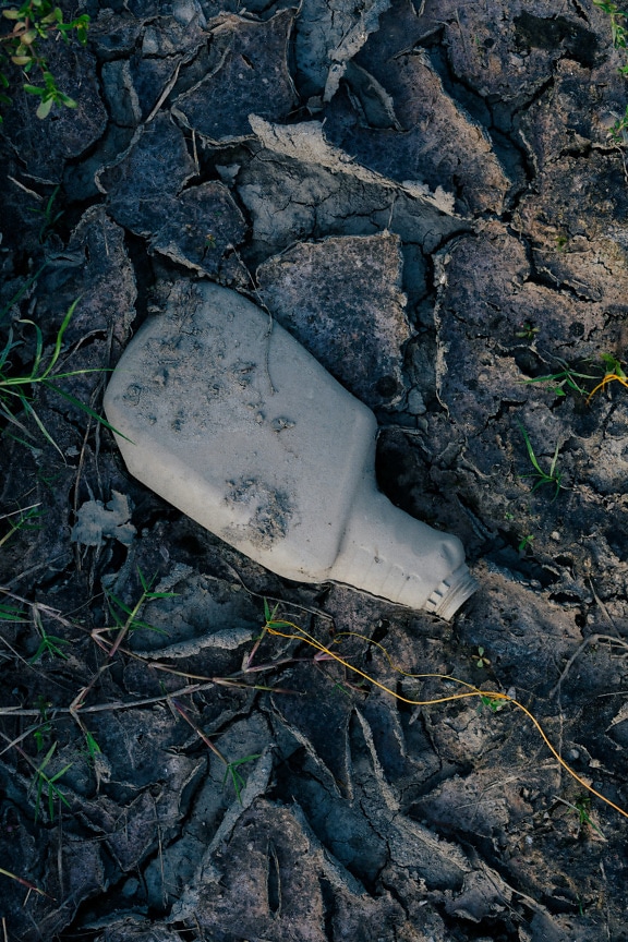Пластиковая мусорная грязно-серая бутылка на сухой почве
