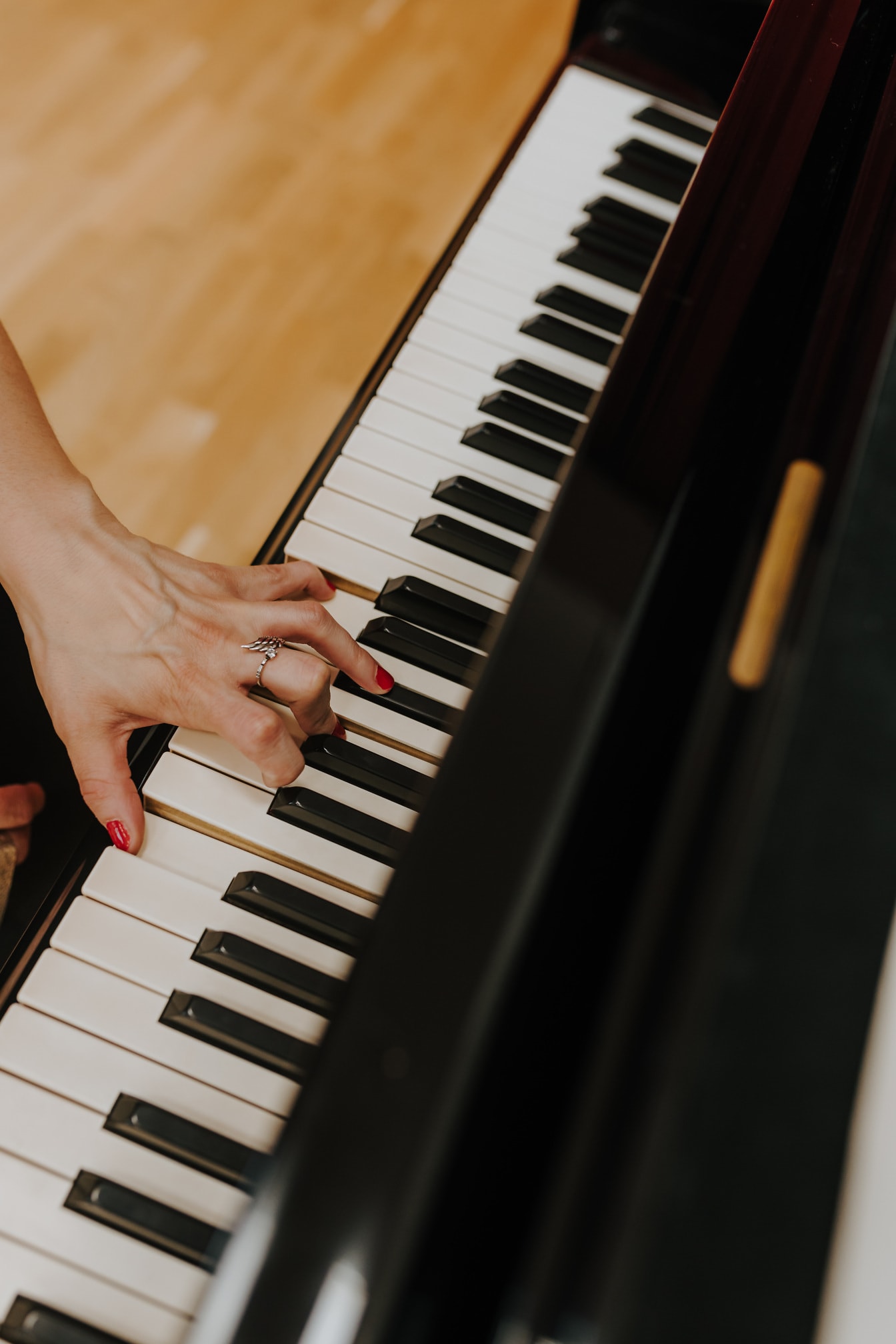 Ruka s prsteňom a červeným lakom na nechty pri hre na klavíri zblízka