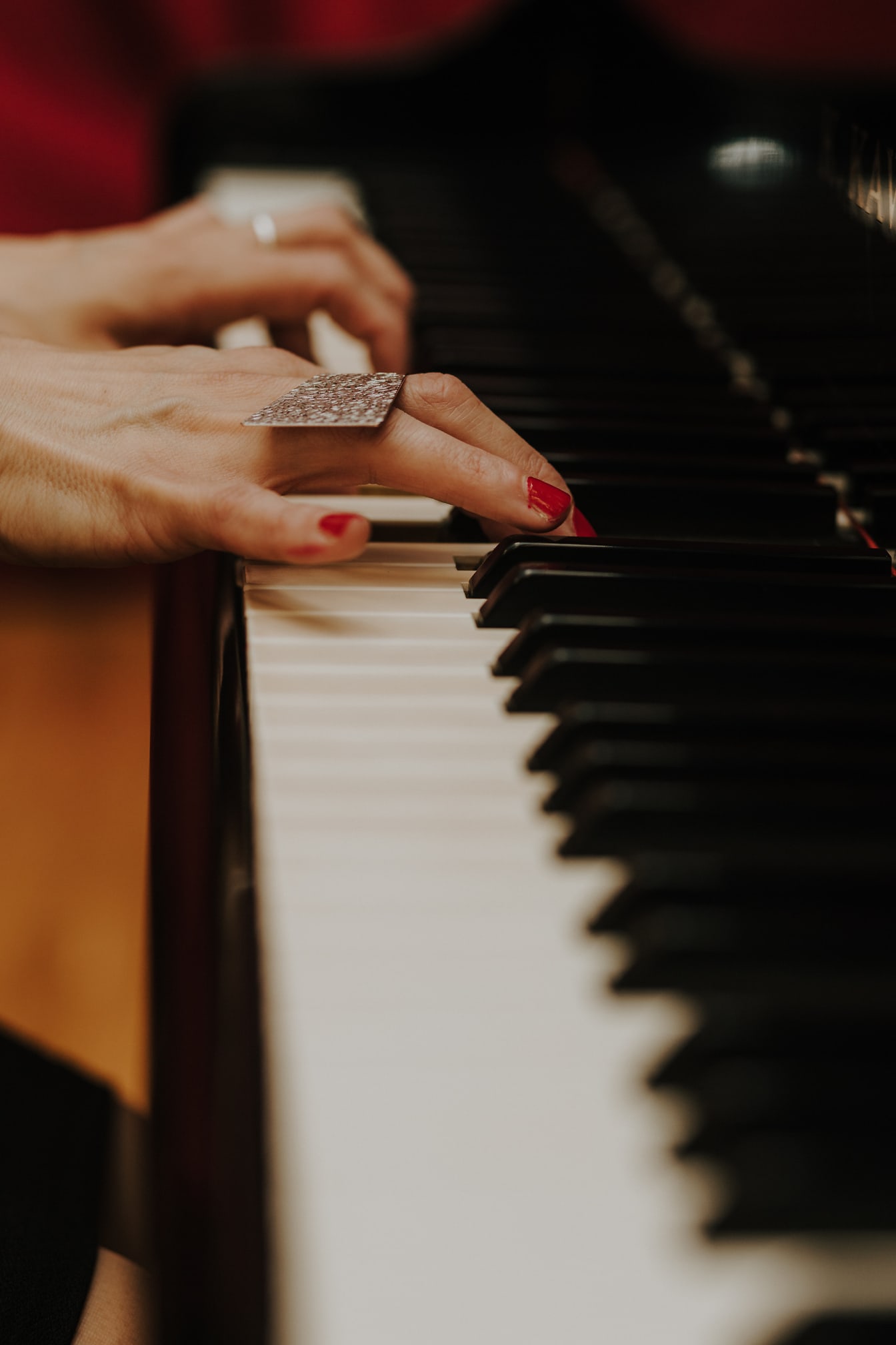 ภาพระยะใกล้ของมือเล่นเปียโนด้วยยาทาเล็บสีแดงที่นิ้ว