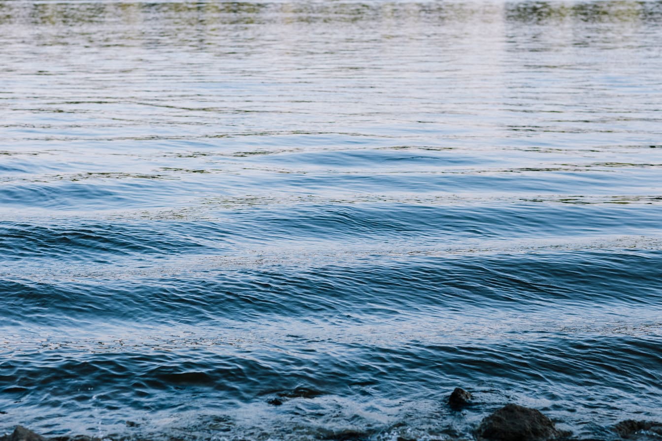 Azurblaue Wellen kräuseln sich am Flussufer