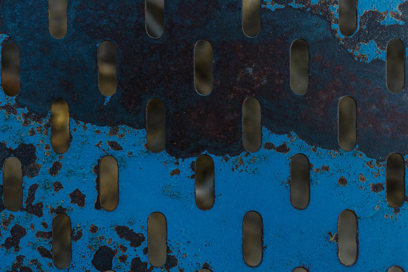 Donkerblauwe verf op roestig metaal met geometrisch gatenpatroon
