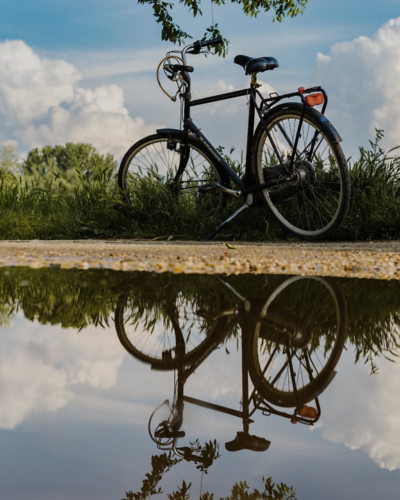 Bicycle on dirt road with reflection on pond