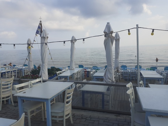 Empty terrace of beachfront restaurant with white chairs and tables