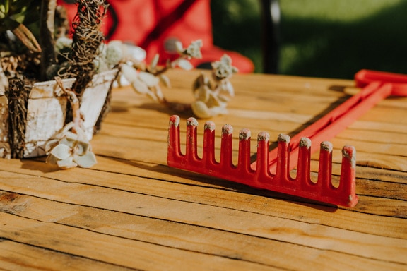 Close-up of dark red plastic toy rake tool on wooden table