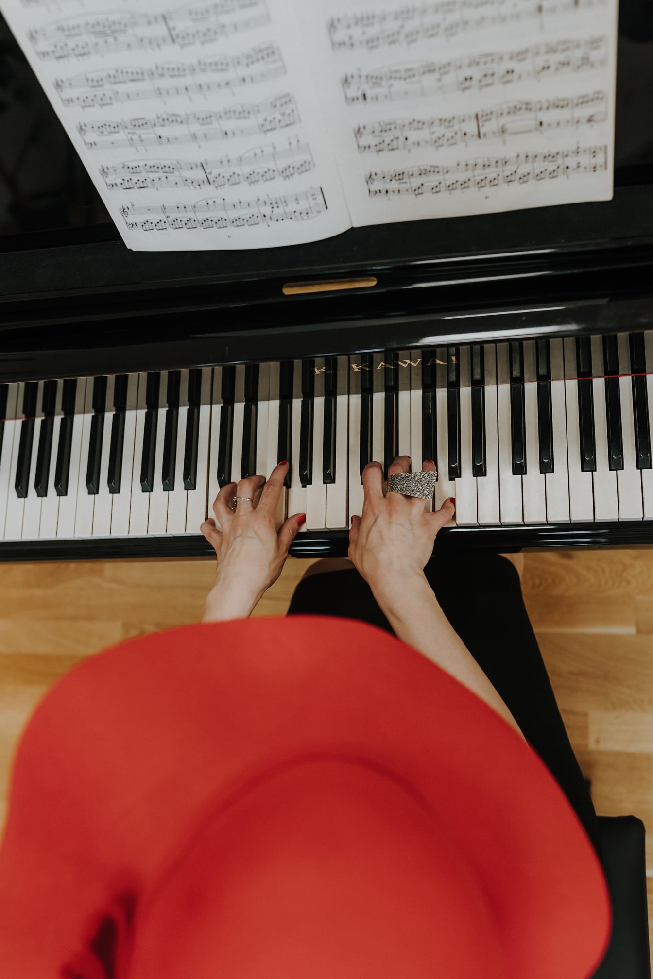 Žena klaviristka s červeným klobúkom hrajúca na klavírny nástroj