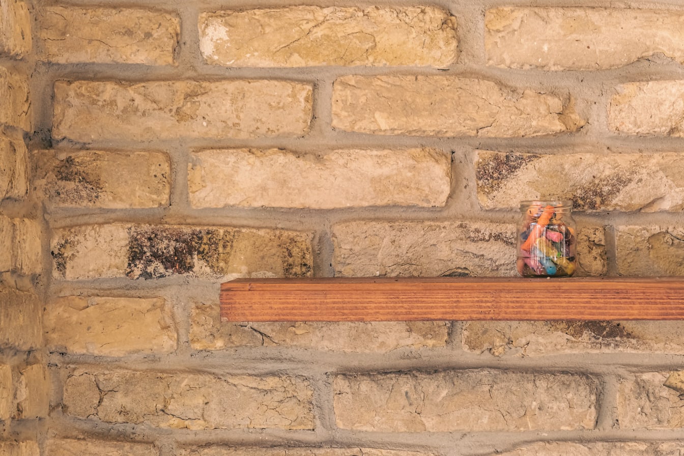 Баночка с разноцветными мелками на деревянной полке на кирпичной стене
