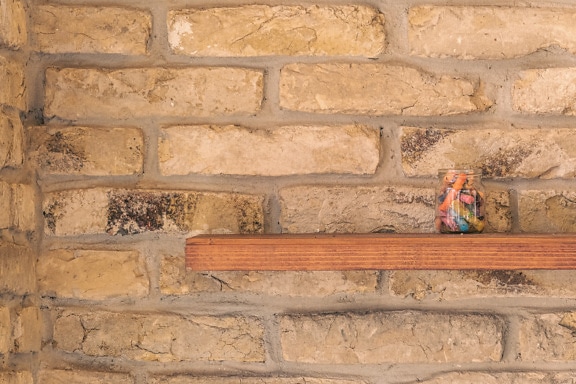 Jar with colorful crayons on wooden shelf on brick wall