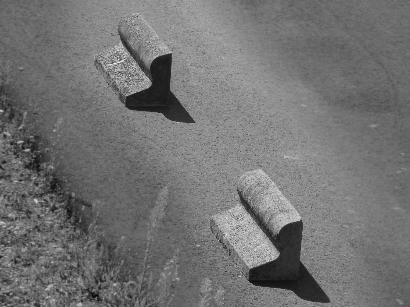 Monochromes Foto von Betonblöcken mit verzerrter Form auf einer Asphaltstraße