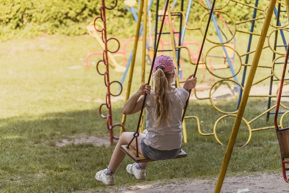 Blonde hair school girl on swing in playground