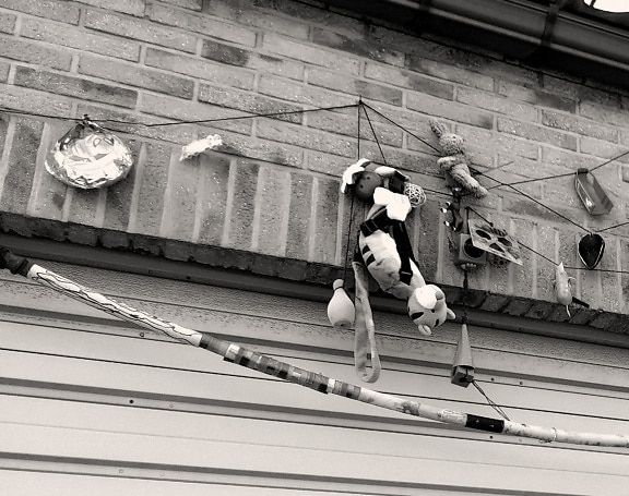 Monochrome photo of hanging toys on rope on brick wall