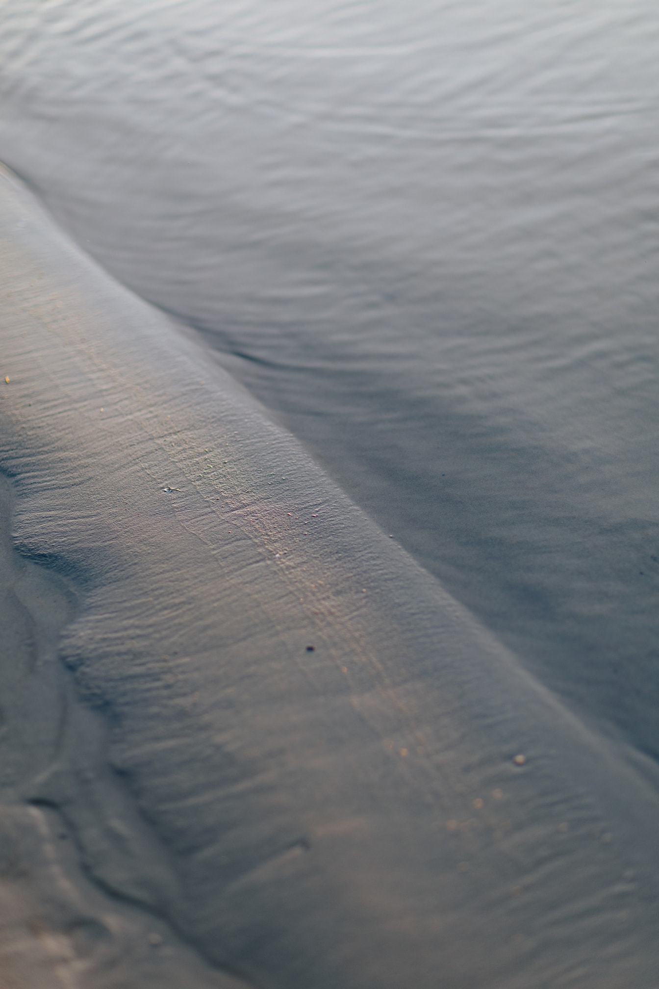 Närbild av våt sand på lugnt vatten på flodstranden