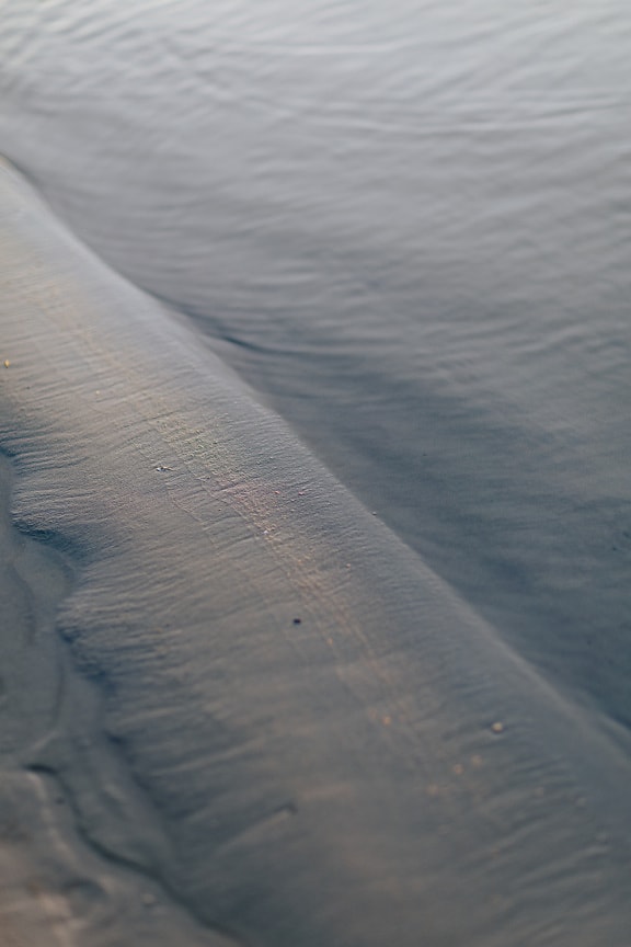 Close-up of wet sand on calm water on riverbank beach