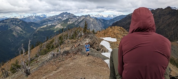Pendaki di jacker merah tua duduk dan menikmati panorama