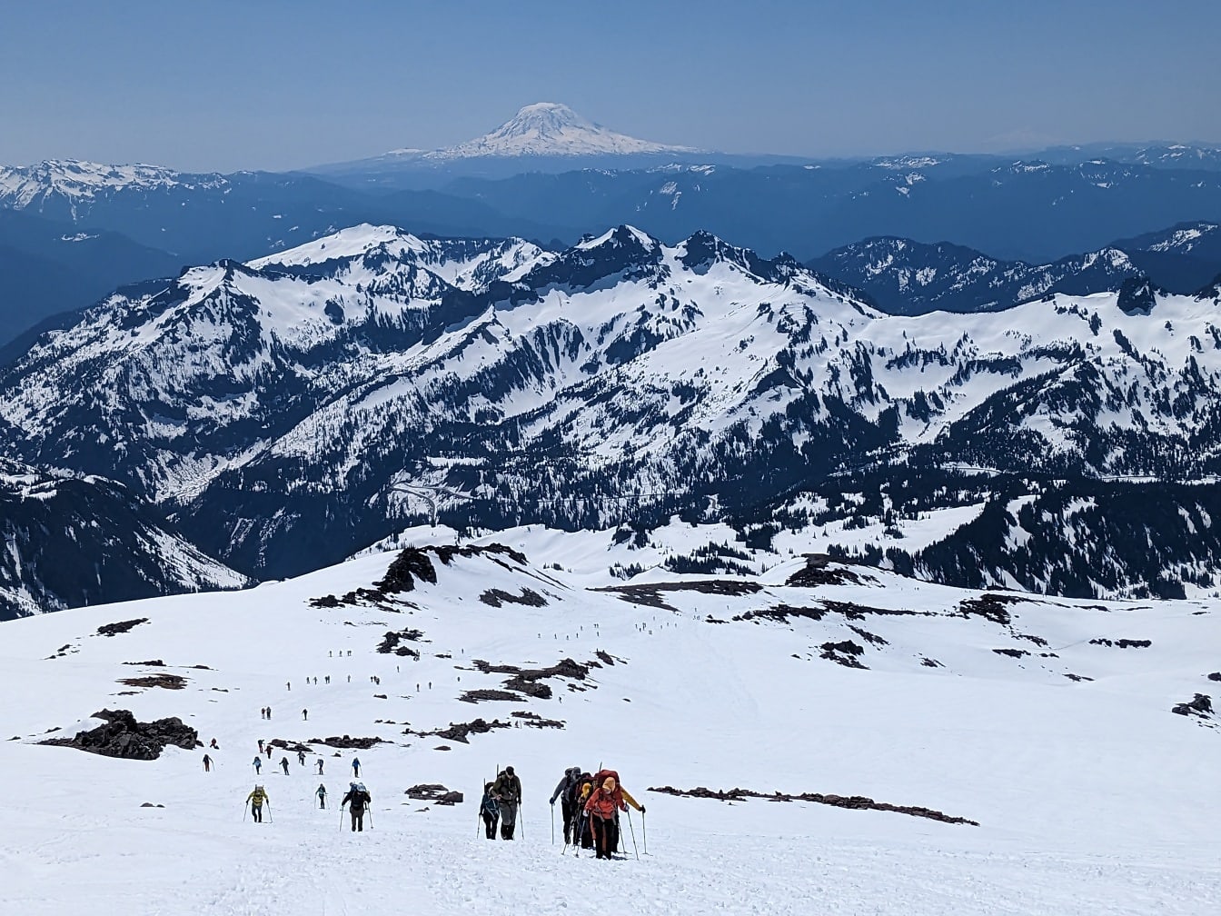 Альпинисты-лыжники, поднимающиеся на заснеженную горную вершину