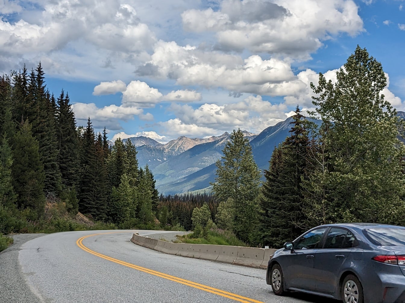 Chiếc xe sedan kim loại màu xanh đậm trên đường nhựa ở sườn núi