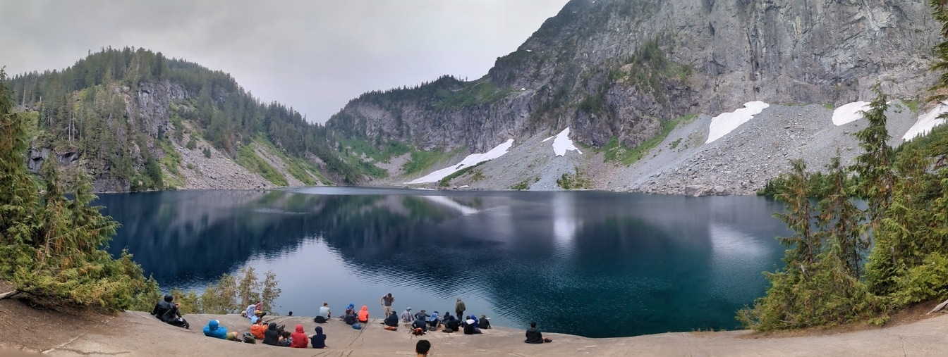 Dav turistů sedících na břehu a užívajících si majestátní břeh jezera