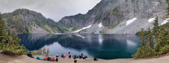 Crowd hikers sitting on shore and enjoying majestic lakeside