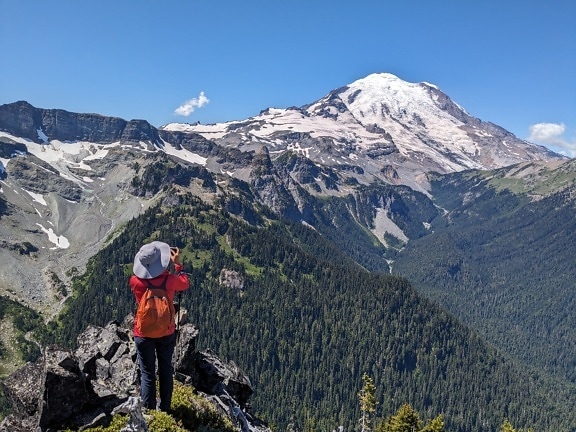 Mountain climber with orange yellow backpack enjoying panorama