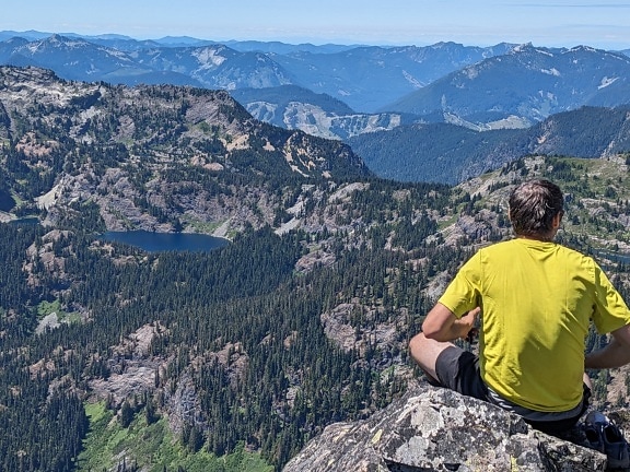 Muž sedí na vrcholu hory a užívá si panoramatický výhled