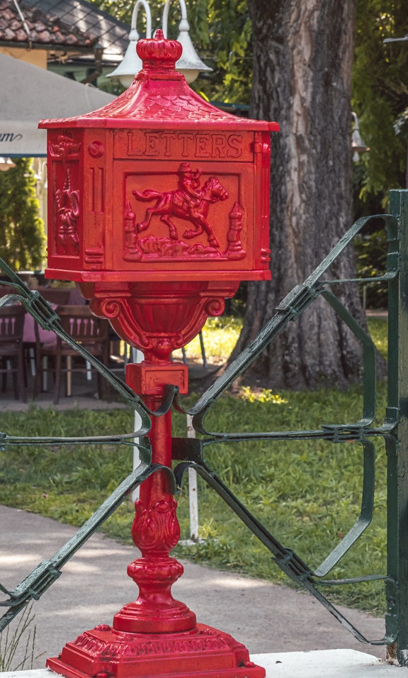 Ciemnoczerwona rustykalna żeliwna skrzynka pocztowa w stylu vintage na ogrodzeniu