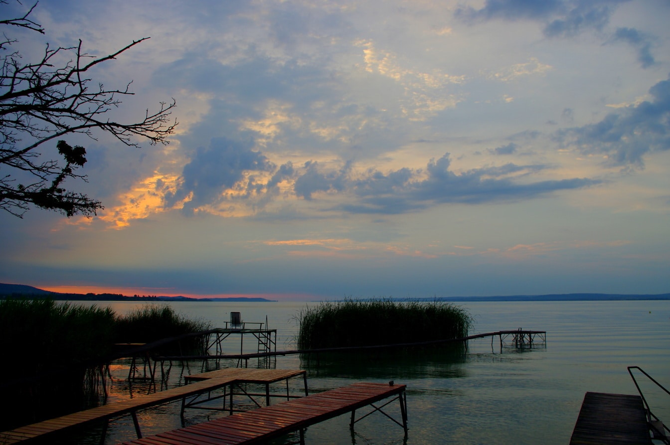 พระอาทิตย์ตกเหนือทะเลสาบ Balaton ในฮังการี ท้องฟ้ายามพลบค่ําในท่าเรือ