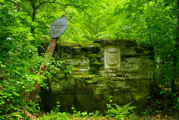 Decay stone monument with sign post overgrown in forest