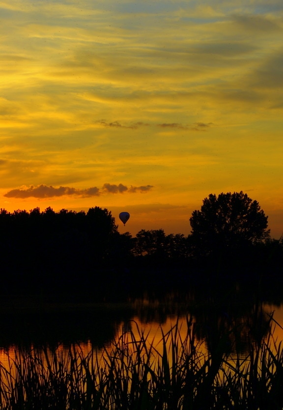 夕暮れ時の湖畔の上空を飛ぶ熱気球のシルエット
