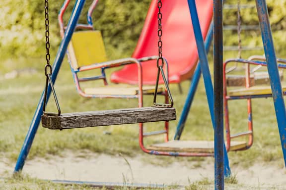 Drevená rustikálna hojdačka zavesená na železnej reťazi na detskom ihrisku