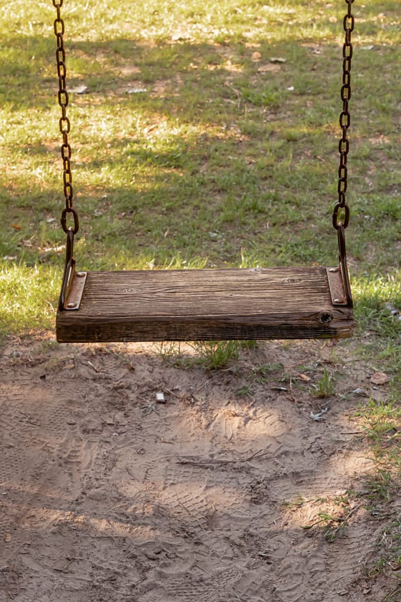 Wooden rustic swing on rust cast iron chain close-up