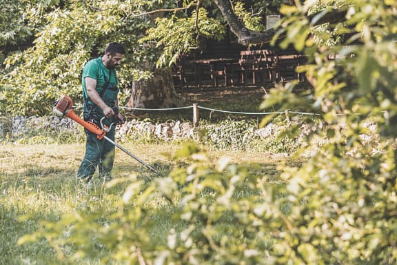 Professionele arbeider die gras in park met trimmer grasmaaier snijdt