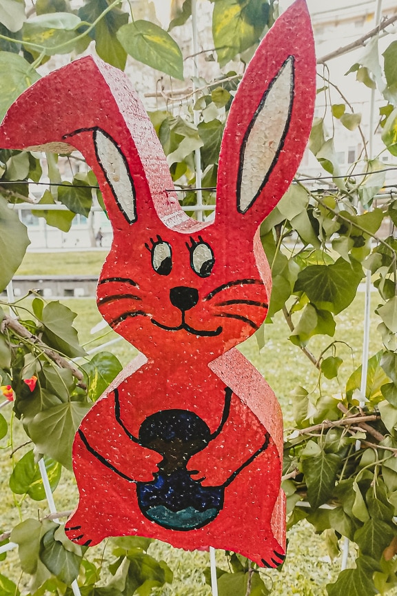 Reddish plastic Easter bunny decoration in green leaves