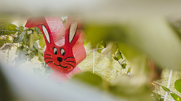 Dark red plastic Easter bunny in greenish yellow leaves